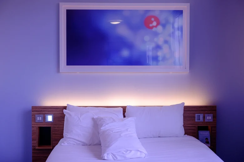 Ein Hotelbett mit zwei Kissen. Über dem Bett hängt ein Bild. Das Foto hat eine gedämpfte Stimmung.