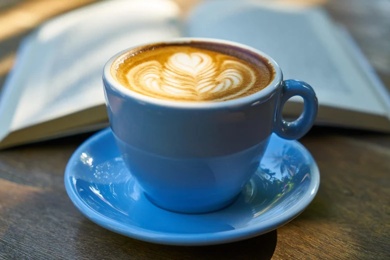 Cappuccinotasse mit Kaffee und Milichschaum steht vor einem aufgeschlagenem Buch